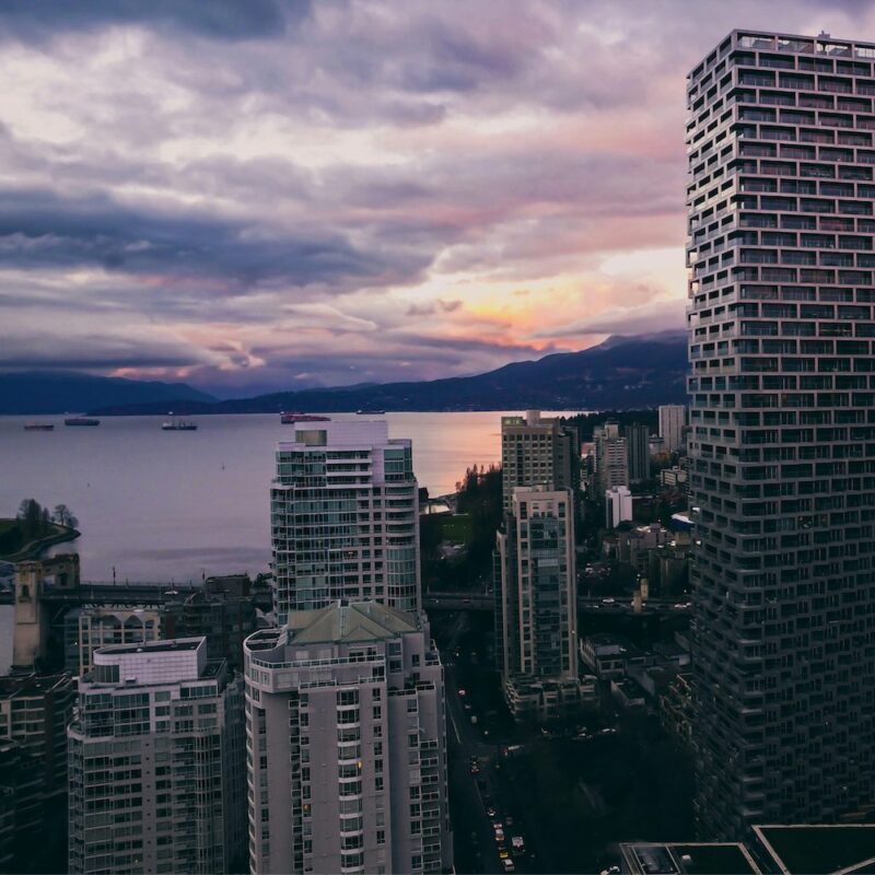 Vancouver skyline with high-rise buildings in the foreground, set against a backdrop of mountains and ocean.